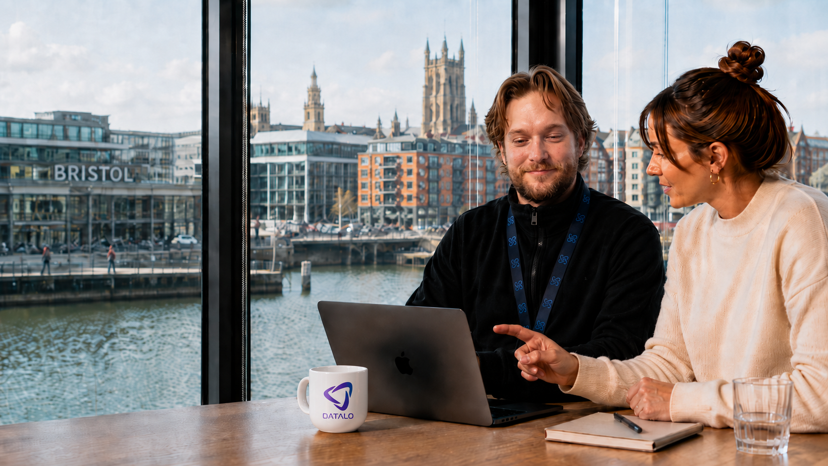 Two Assured Digital consultants reviewing work together on a laptop in a modern Bristol office overlooking the harbourside